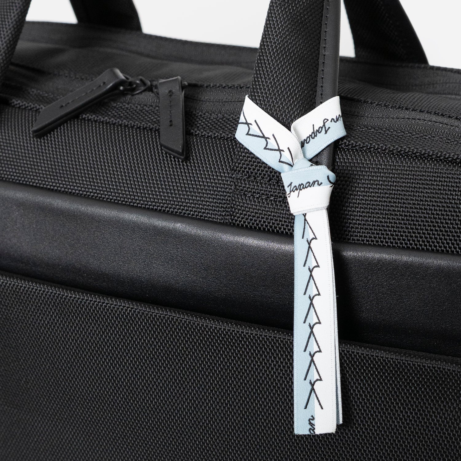 Floe ワーク＆デイリーブリーフケースはメイドインジャパン・日本製の証が付いています。ブランドマークの”y”を連ねたリボンのデザインで、北海道の空と雪のカラーを取り合わせました。リボンは外してお使いいただくことも可能です。