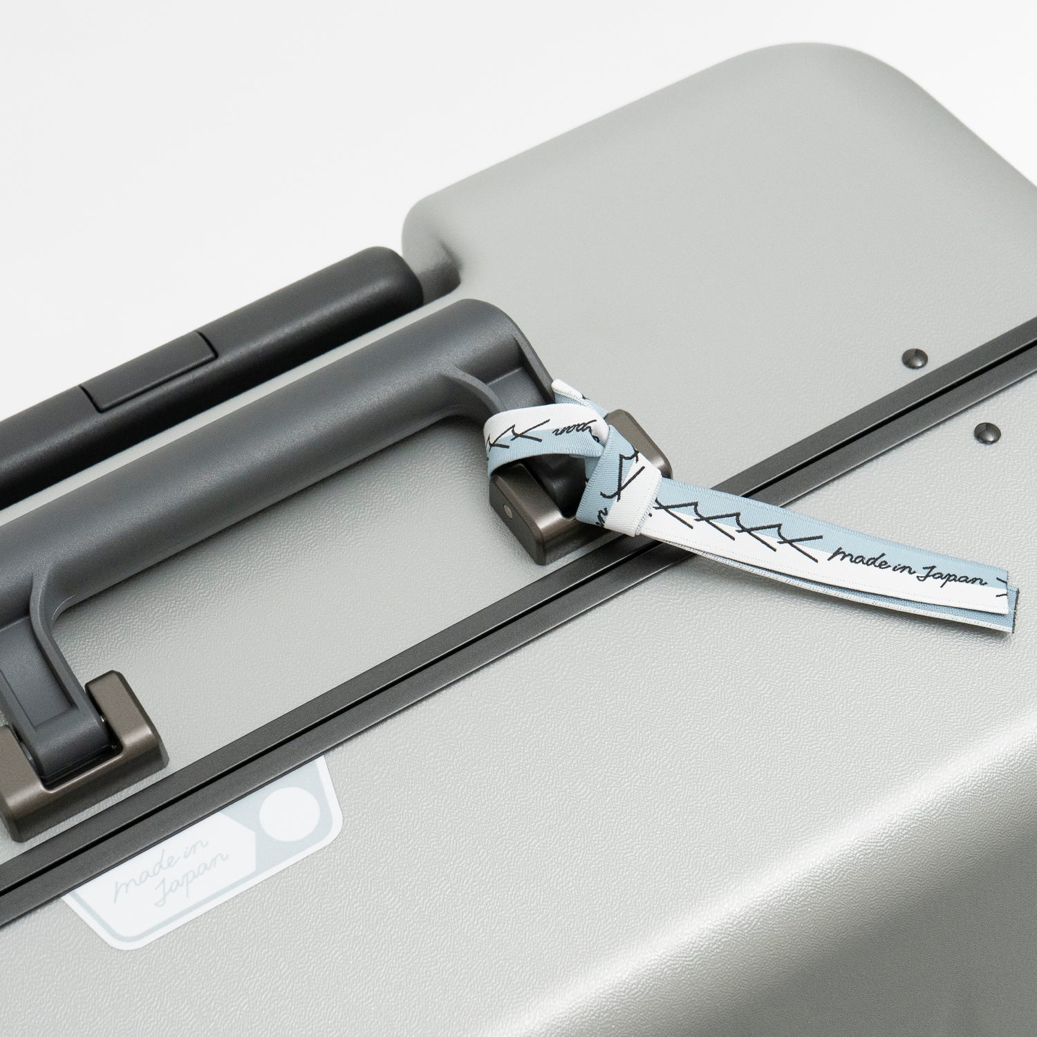 アイシクル フレームスーツケース（キャリーケース）のメイドインジャパン・日本製の証。エースラゲージ北海道赤平工場から望む、イルムケップ山と太陽をモチーフにしています。リボンはブランドマークの”y”を連ねたデザインで、北海道の空と雪のカラーを取り合わせました。シールとリボンは、剥がしてお使いいただくことも可能です。