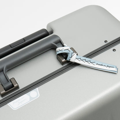 アイシクル フレームスーツケース（キャリーケース）のメイドインジャパン・日本製の証。エースラゲージ北海道赤平工場から望む、イルムケップ山と太陽をモチーフにしています。リボンはブランドマークの”y”を連ねたデザインで、北海道の空と雪のカラーを取り合わせました。シールとリボンは、剥がしてお使いいただくことも可能です。